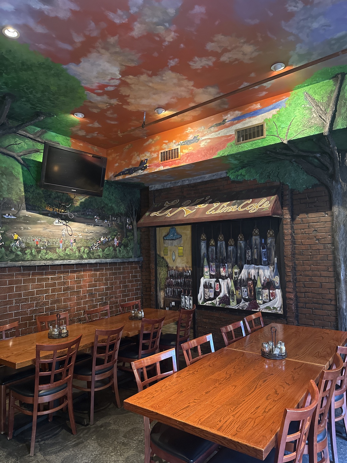 The wine-cafe corner mural at Ferraro's — painted wine bottles under an awning, beneath a ceiling of sunset clouds and jets
